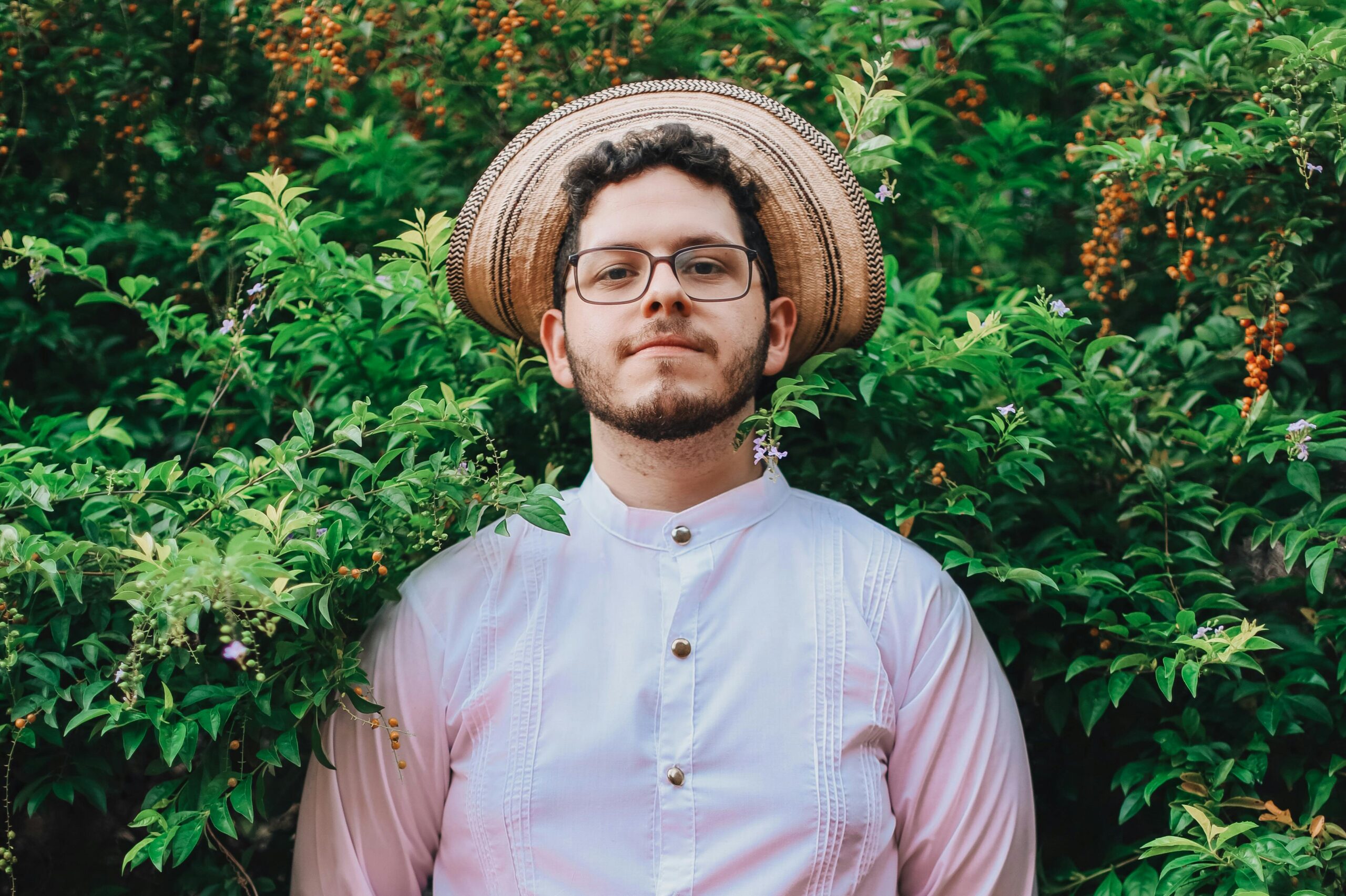 A Man in a Shirt and Hat Standing on the Background of a Shrub